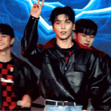 a man in a black leather jacket is giving a peace sign while standing in front of two other men .