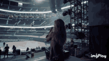 a woman singing into a microphone in an empty stadium with imgplay written below her