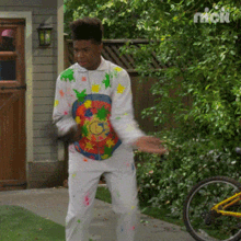 a man in a colorful shirt and white pants is standing in front of a bicycle