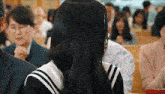 a woman with long black hair is sitting in a crowded room with people praying .