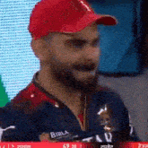 a man wearing a red hat and a blue shirt with the word birla on it is making a funny face .