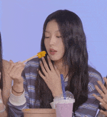 a girl is eating a piece of food with chopsticks and a cup of milk