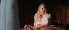 a woman sitting on a bed with a red blanket