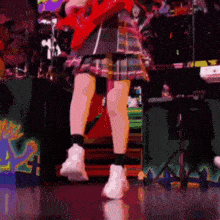 a girl in a plaid skirt is playing a red guitar on stage