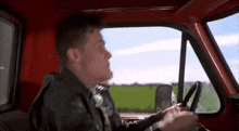 a man is driving a red truck on a road .