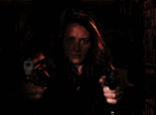a woman in a leather jacket is pointing two guns