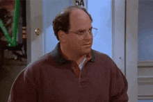 a bald man wearing glasses and a sweater is standing in front of a door .