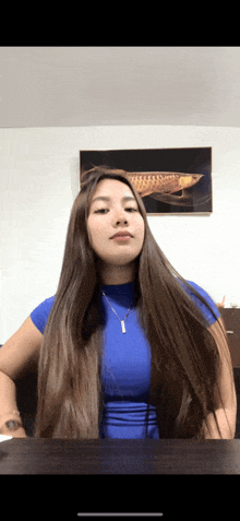 a woman with long hair is sitting at a table with a picture of a fish on the wall behind her
