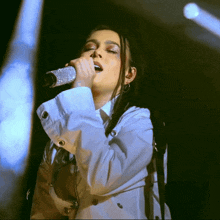 a woman singing into a microphone while wearing a white coat