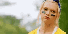 a close up of a woman wearing a yellow shirt and a blue headband with a black patch on her face .