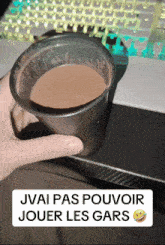 a person holding a cup of chocolate next to a keyboard that says j'ai pas pouvoir jouer les gars