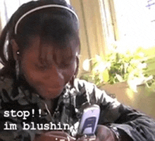 a woman wearing headphones and a headband is looking at her cell phone with the words stop i 'm blushing below her