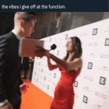 a woman in a red dress is talking into a microphone while a man in a suit looks on
