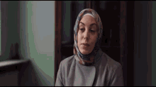 a woman wearing a hijab and a grey coat looks at the camera
