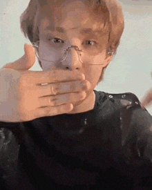 a man with glasses is covering his mouth with his hand .