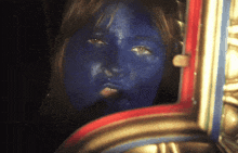 a woman with blue paint on her face looks at herself in the mirror