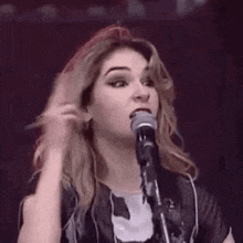 a woman is singing into a microphone and pointing at her head .