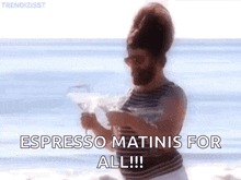 a man with a beard is standing on a beach holding a martini .