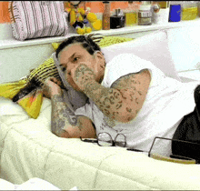 a man with a tattoo on his arm is laying on a bed with glasses