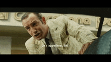 a man in a suit and tie is standing in front of a sign that says " je t 'appellerai bill "