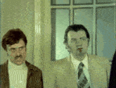 two men in suits and ties are standing next to each other and one has a cigarette in his mouth