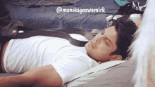 a man laying on a bed with a belt around his neck and the name monikagoswamirk on the bottom right