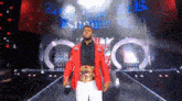a man in a red jacket and white pants is standing on a stage holding a microphone