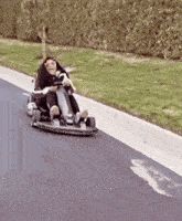 a person is riding a go kart down a road while holding a remote control .