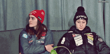 a girl wearing a gornje hat sits next to another girl on a couch