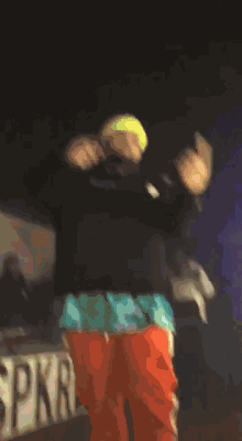 a man wearing a neon yellow hat and orange pants is dancing on stage