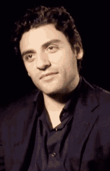 a close up of a man 's face in a suit and black shirt