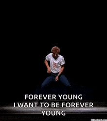 a man is jumping in the air on a stage with the words `` forever young i want to be forever young '' written on it .