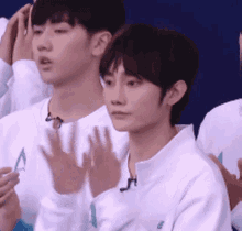 a group of young men wearing white sweaters are clapping their hands .