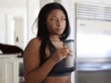 a woman is standing in a kitchen holding a blender and a cup of coffee .