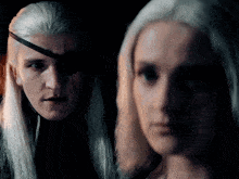 a man with a bandage on his eye is standing next to a woman with long white hair