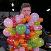 a man is holding a bunch of colorful balloons in front of a sign that says tyrannosaurusmaxy