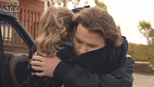 a man and a girl hugging in front of a car that says son of a glitch on it