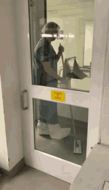 a person standing in front of a door that has a yellow sign on it that says wet floor