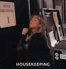 a woman is standing in front of a sign that says star dressing 1 and a box that says housekeeping .