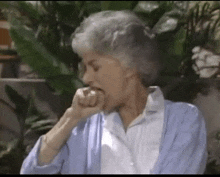 an elderly woman in a blue cardigan is biting her nails .