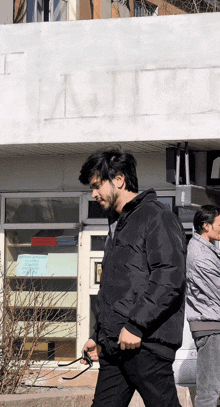 a man in a black jacket is walking in front of a building that says t.
