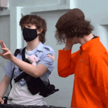 a man wearing a mask is standing next to another man in an orange shirt