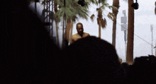 a man in a yellow shirt is standing in front of palm trees