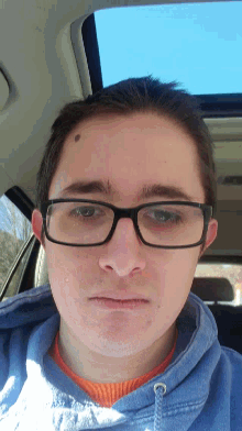 a young man wearing glasses and a blue sweatshirt looks at the camera