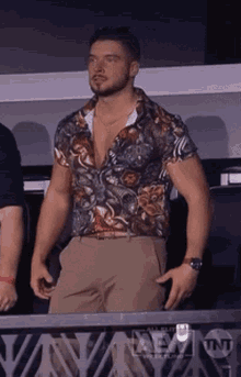 a man in a floral shirt and khaki pants stands in front of a sign that says aem