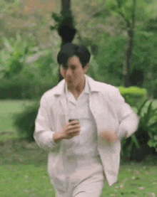 a man in a white suit is running in a park .
