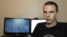 a man in a black shirt is sitting in front of two computer monitors .