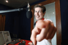 a man is pointing at the camera in front of a microphone and a laptop