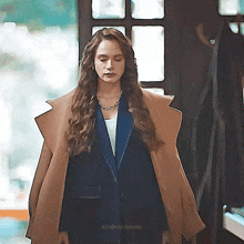 a woman wearing a tan coat and a blue suit is standing in front of a door .