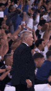 a man in a suit stands in front of a crowd of people with their arms in the air